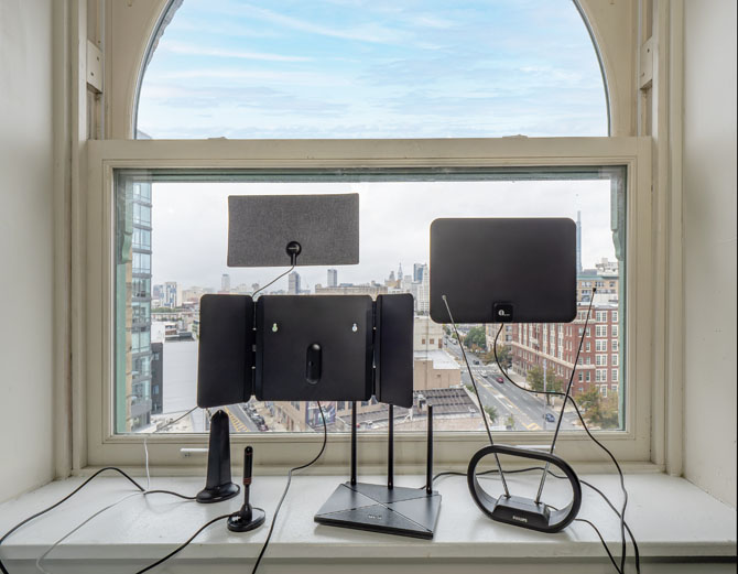 Antennas sitting in a picture window from the top left: Philips Fabric Swatch TV Antenna, 1byone Amplified Indoor Antenna, Philips HD Loop, RCA Amplified Indoor Antenna, Luxtronic Portable TV Antenna with Magnetic Base, XFIREE Digital TV Antenna, and 1byone Model 2 TV Antenna.