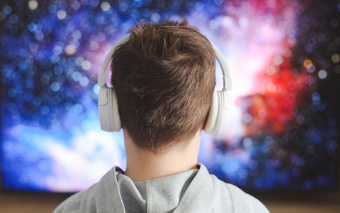 Boy watching TV with headphones show from behind the boy and looking at the TV.