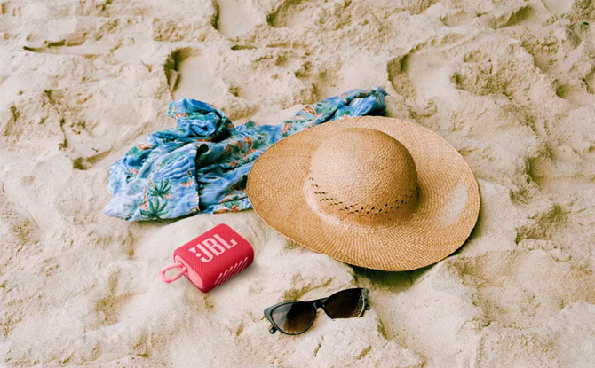 JBL Go 3 on sand with sun hat, tropical print fabric, and sun glasses.