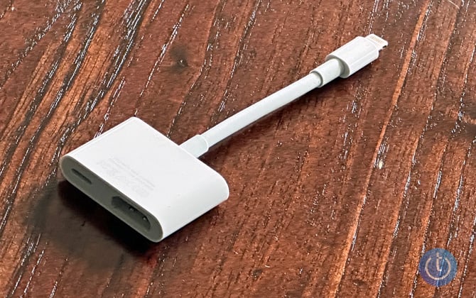 Apple Lightning to HDMI adapter with passthrough port for charging sitting on wood table. Show from the side with the HDMI port.. 