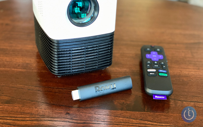 Roku Streaming Stick 4K showing the streaming stick and remote on wood table with mini projector
