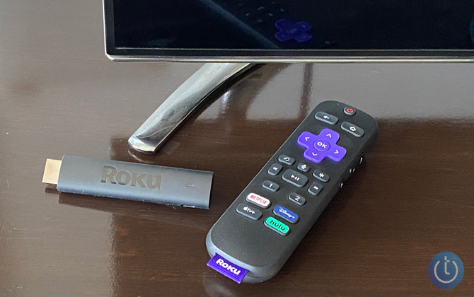 Roku Streaming Stick 4K+ with remote control on wooden table with TV