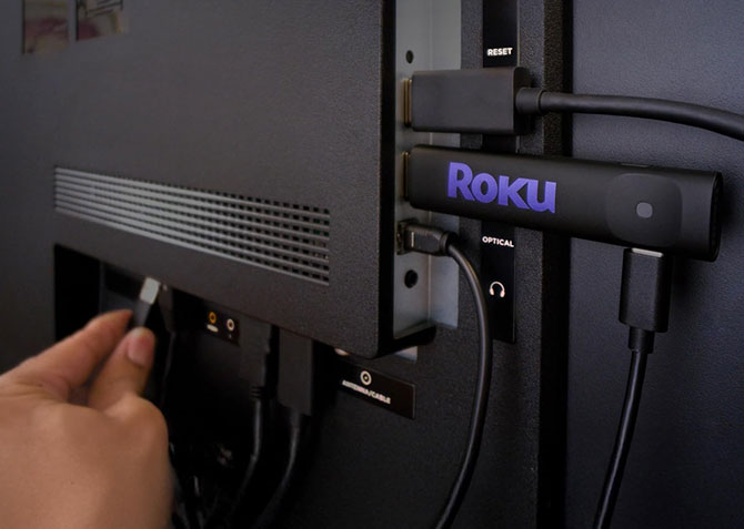Roku Streaming Stick HD being plugged into the back of a TV