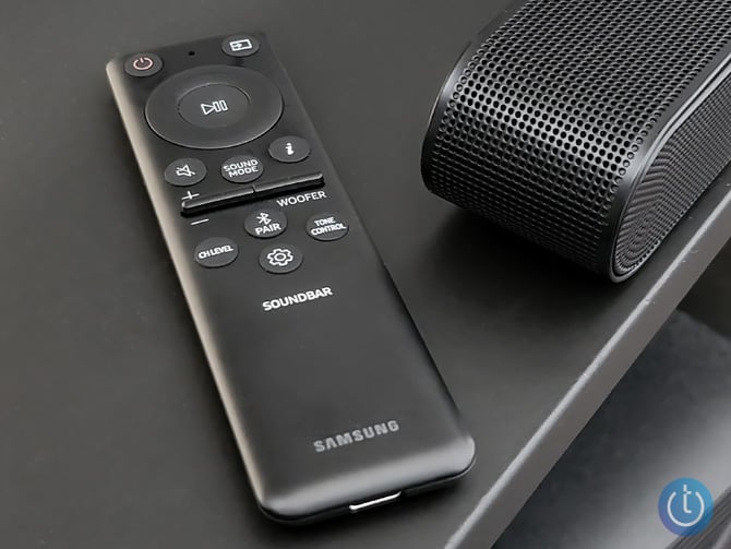 Samsung S800B Ultra-Slim shown from the right end with remote control. On the remote are buttons for power, play/pause, sound model volume up/down, mute, woofer, Channel Level, Bluetooth Pairing, Tone Control and Settings