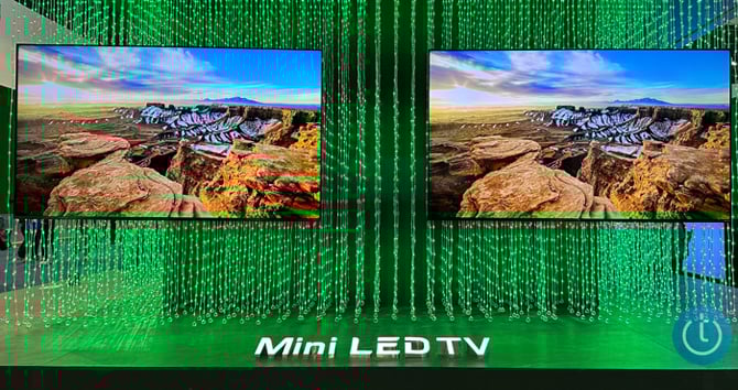 Two TCL Mini LED TVs shown at the TCL booth at CES. Green string lights are behind the two TVs. At the bottom you see: Mini LED TV 