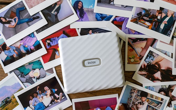 Fujifilm Instax Link Wide Bluetooth printer on top of a pile of prints.