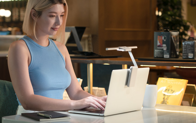 Woman using a laptop with a white BenQ LaptopBar in a cafe.