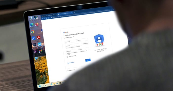 Google account creation screen on laptop on wood surface with a person sitting in front seen in shadow from behind.