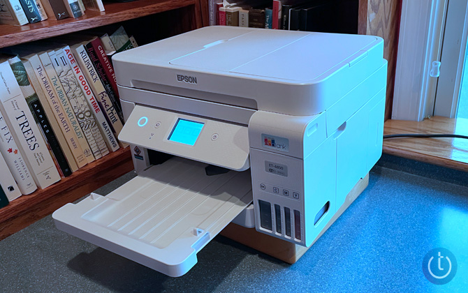 Epson EcoTank ET-4850 shown three quarters in front of a window on a desk and to the right of a bookcase