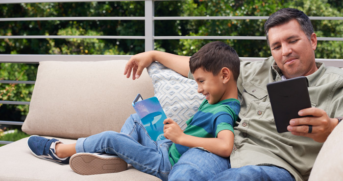 Father and son holding Kindle 11th gen and Kindle Kids 11th gen with Space Whale on a porch with trees in the background.