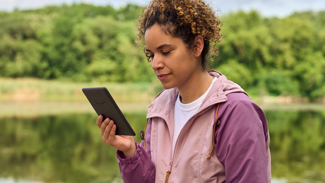 Woman reading on a Kindle Paperwhite next to a lake