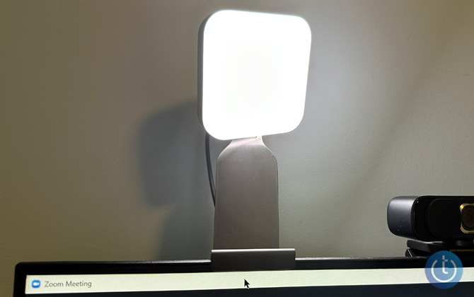 Litra Glow with the light turned on mounted on a computer monitor next to a web cam.