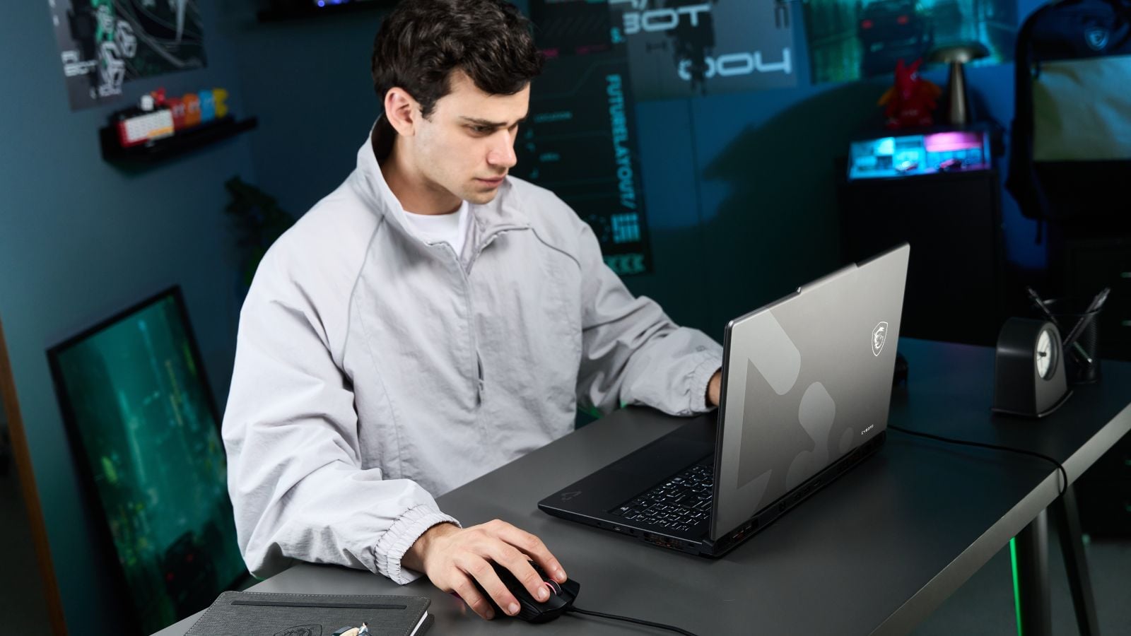Man using an MSI Cyborg 15 gaming laptop and a wired mouse at a dark desk in a gaming room with neon-lit decor