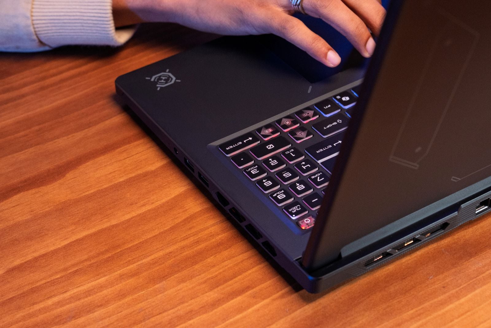 Close-up of the MSI Crosshair A16 HX's backlit number pad and left-side ports, with a hand resting on the touchpad.