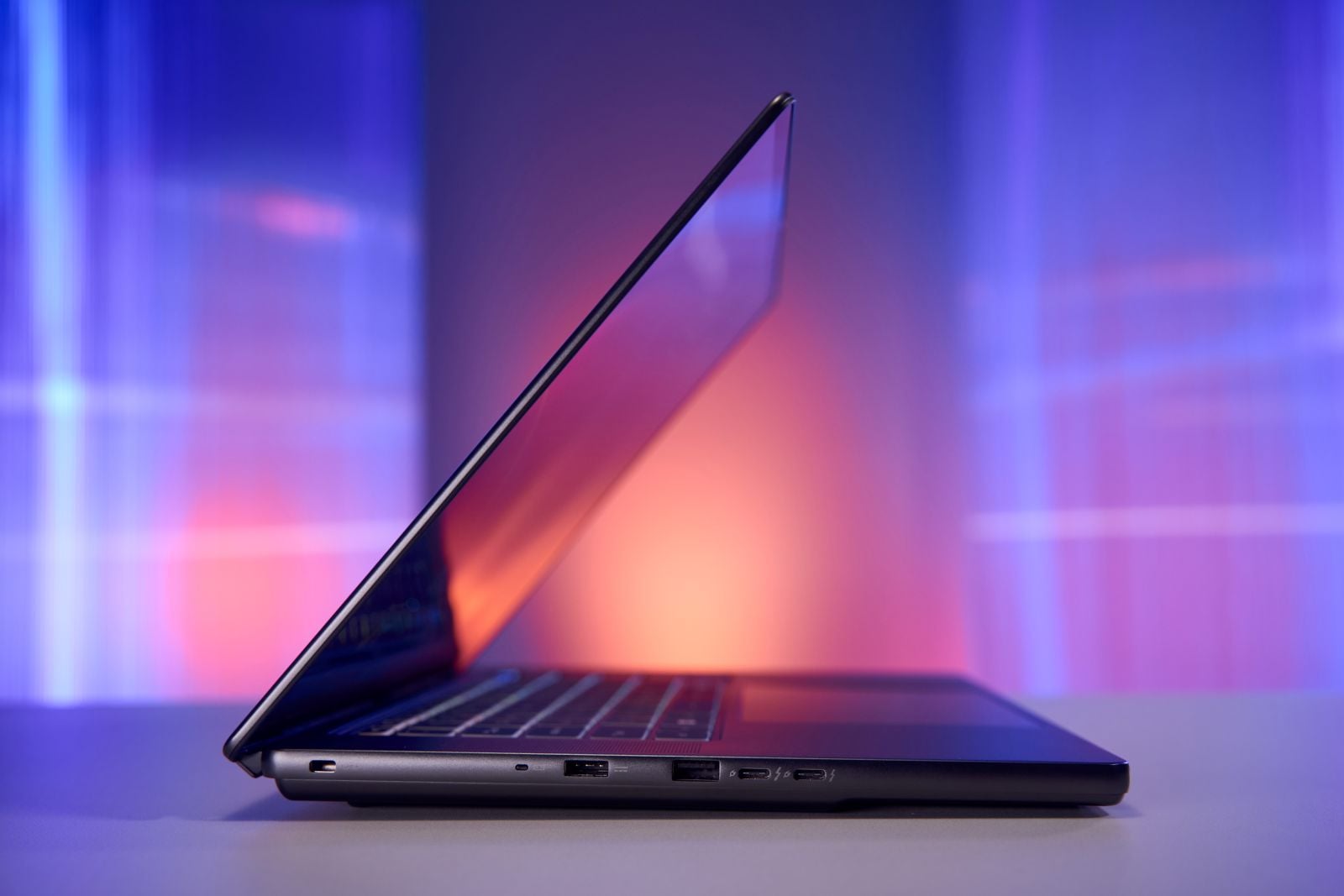 Side view of the MSI Stealth 16 AI+ with the lid open, showing its thin profile, a lock slot, two USB-A ports and two USB-C ports against a purple and orange backdrop.