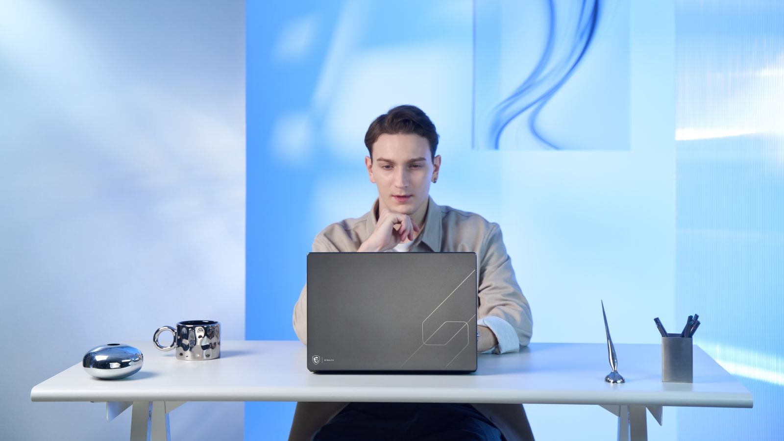 A man works at a white desk behind a closed MSI Stealth 16 AI+, its charcoal aluminum lid marked with a subtle geometric design and Stealth logo.