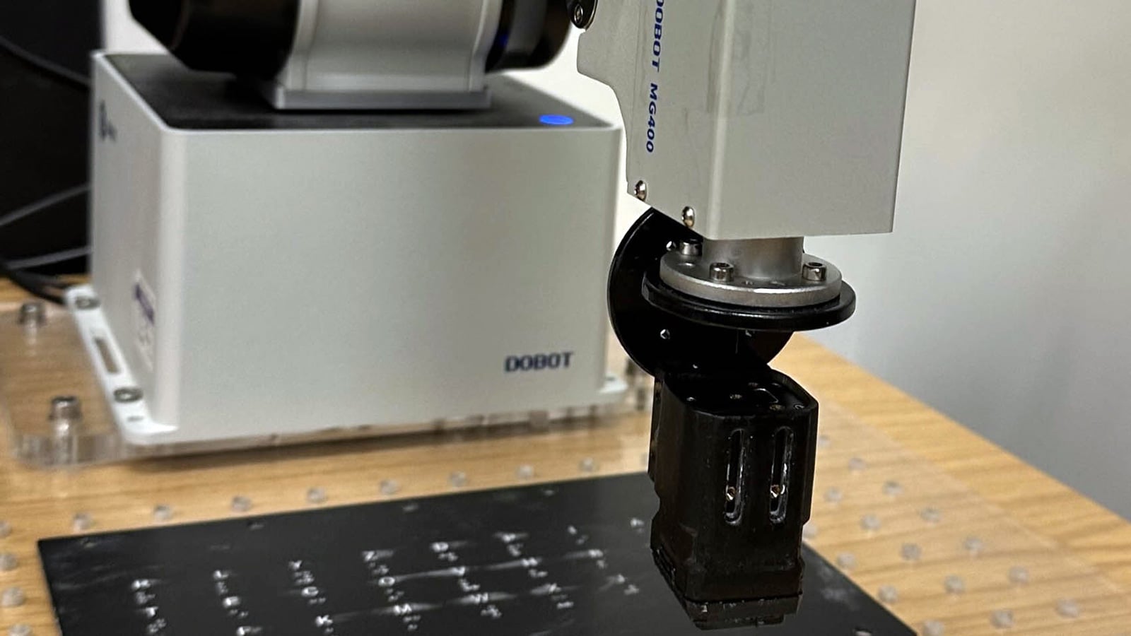 Robotic arm with a black tactile sensor positioned over raised Braille dots on a black test panel.