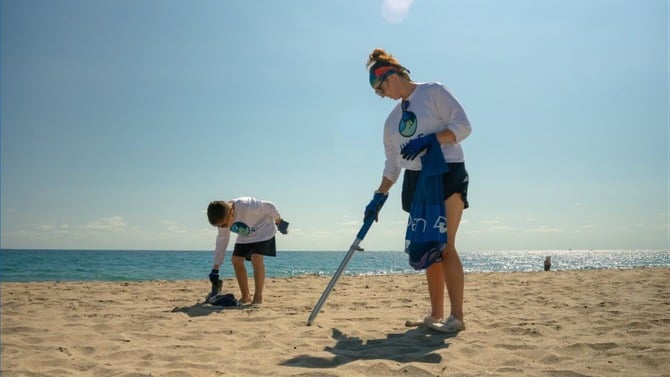 Two people on a beach cleaning garbage wearing tshirts with wave browser logo
