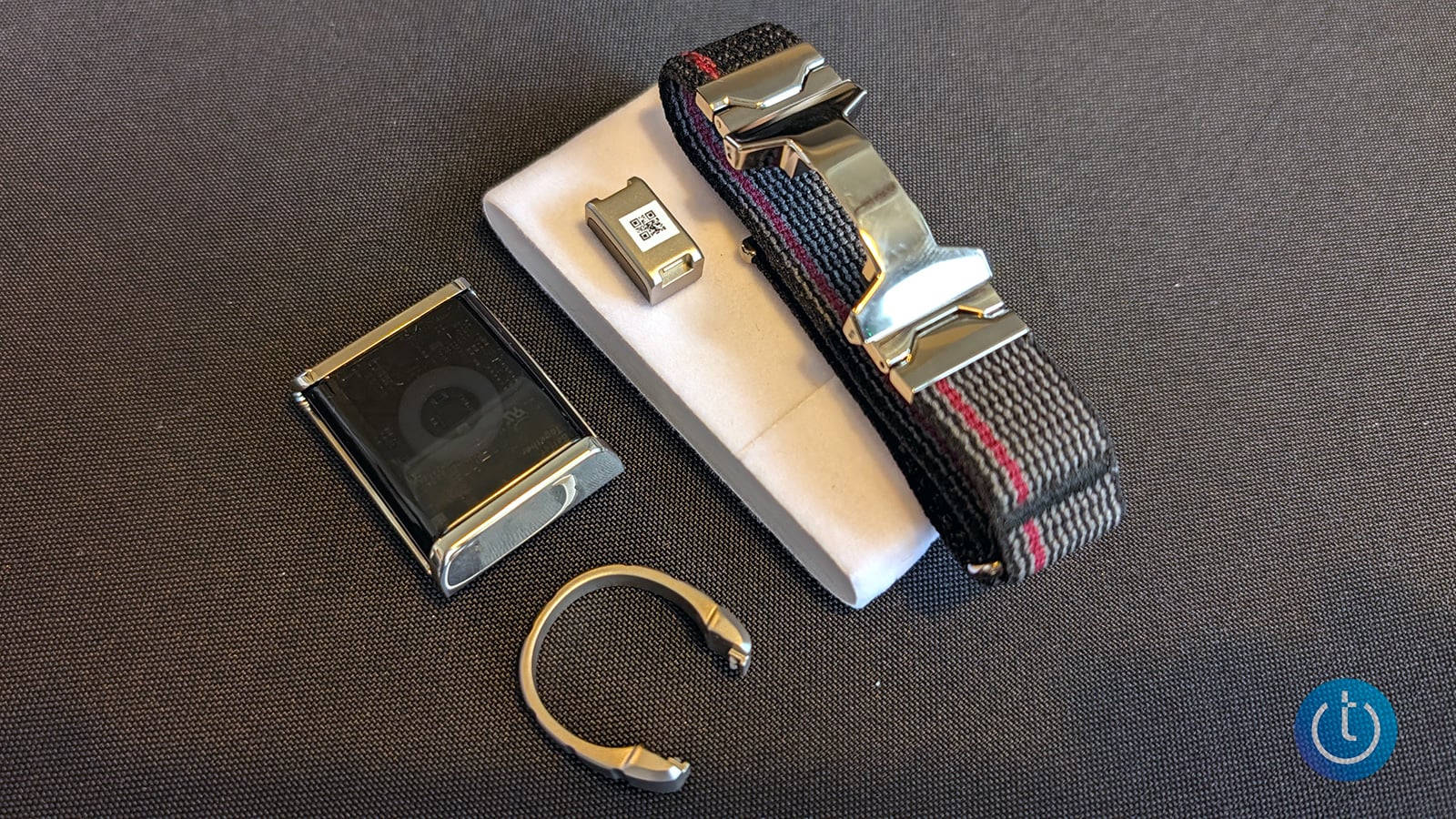Alloop Trio components arranged on gray fabric: a Cube sensor module, Halo accessory, woven wristband with a metal mount, and open metal ring.