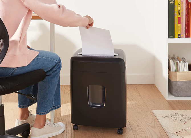 AmazonBasics 12-sheet Micro-Cut Shredder shown with a woman feeding it a sheet of paper.