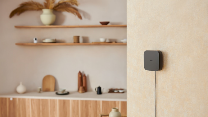 Aqara Hub M3 in black shown attached to a wall with cord below