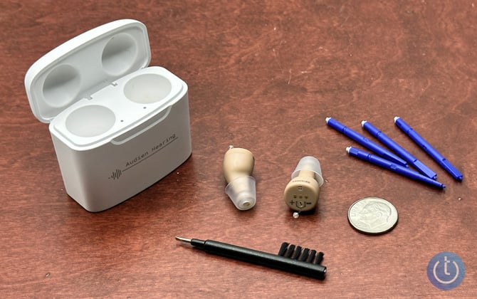 Audien Atom Pro shown with their case, the brush/screwdriver tool, blue sticks with wax guard replacements, and a dime for scale.