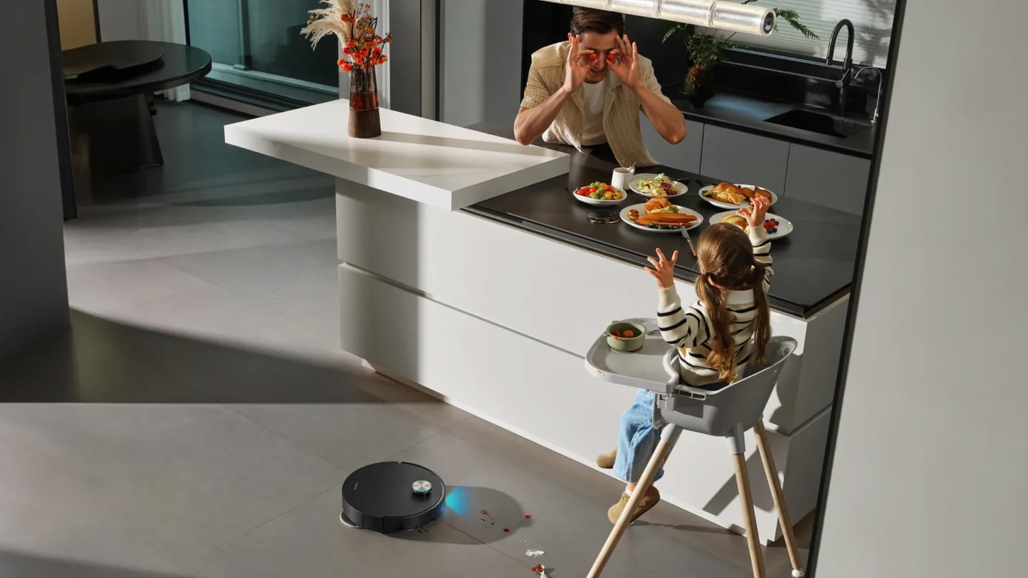 Dreame X60 Ultra robot vacuum cleaning a kitchen floor while a parent and child eat at the island.