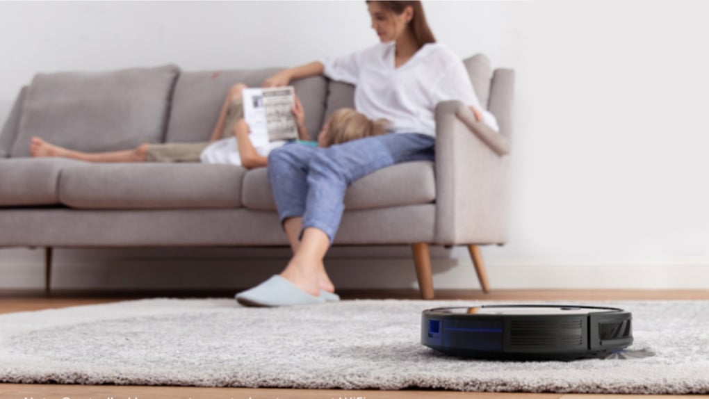Eufy E25 robot vacuum cleaning a rug in front of a woman relaxing on a sofa.