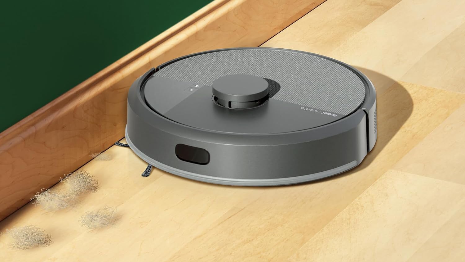 Roomba 105 Combo robot vacuum approaching dirt on a wood floor beside a baseboard.