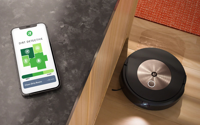 iRobot Roomba Combo j9+ shown vacuuming a floor with a phone showing a screenshot of the Dirt Detective Interface. You can see varying shades of green for the rooms to indicate how clean they are.
