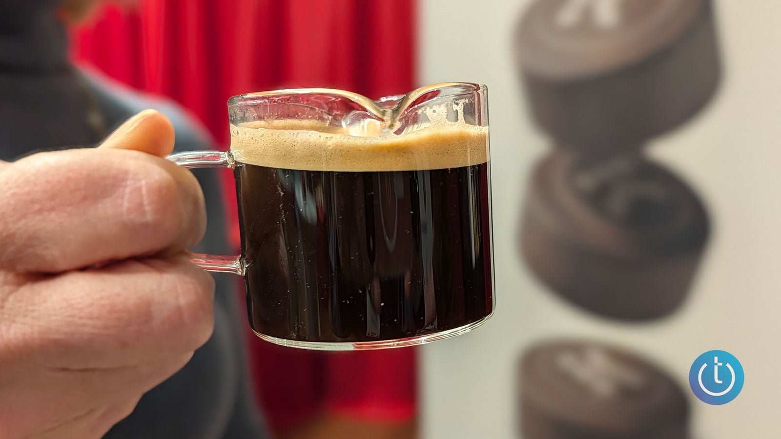A hand holds a glass cup of dark espresso topped with a thick layer of golden crema brewed by the Keurig Alta.
