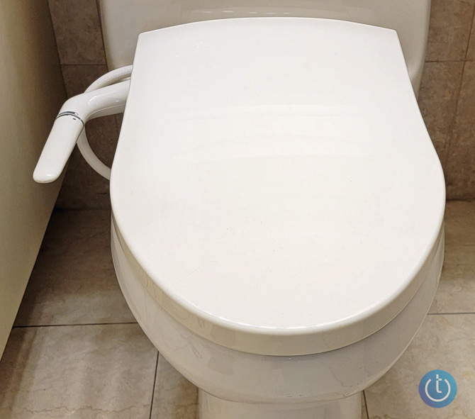 Kohler Puretide bidet installed on toilet seen from the top down. You can see a marble wall in back and the side of a cabinet.