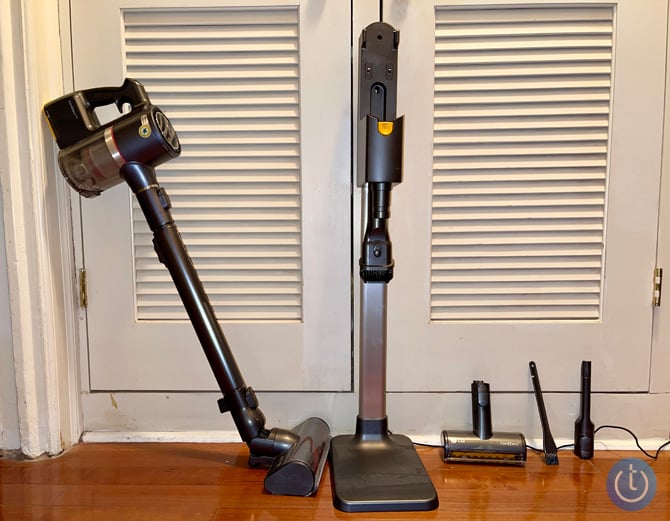 LG CordZero A9 Ultimate propped up against a closet to the left of its charging station. On the floor to the right of the charging station are the Power Punch Nozzle, crevice tool, and 2-in-1 extending combo tool for dusting. 