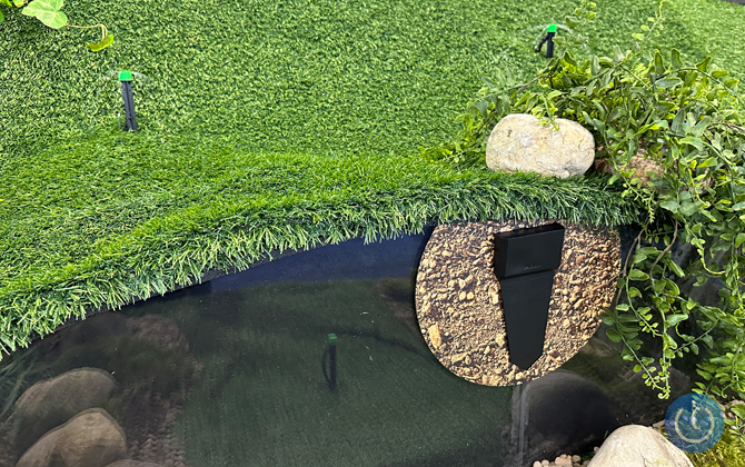 Artificial turf with sprinkler heads and vines with a cutaway showing the Moen Smart Wireless Soil Sensor in rocky soil. 