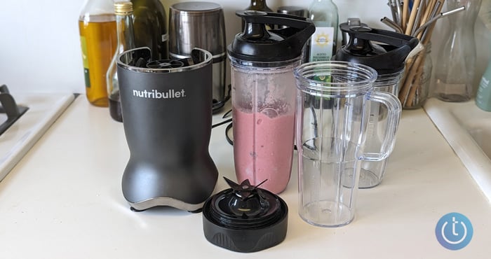 Nutribullet with its three blending cups and two lids. One of the cups holds a strawberry smoothie.