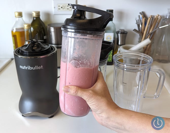 Nutribullet Ultra base with a cup filled with strawberry smoothie held in a hand. 