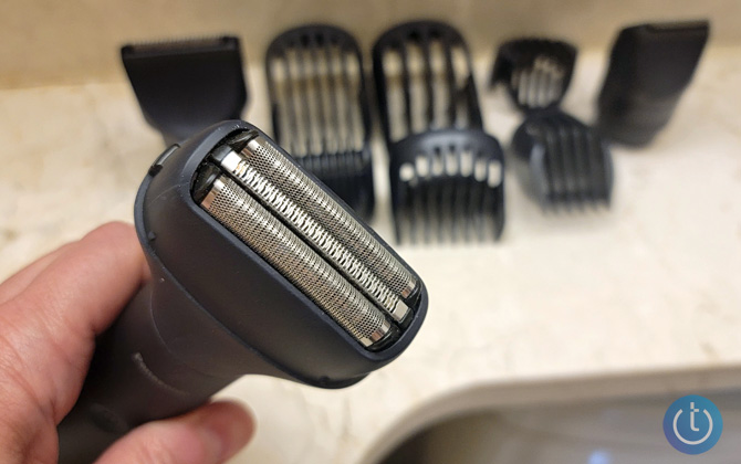 Panasonic Multishape held in hand with shaver attachment. Blurred in the background are the trimmer heads and attachements.