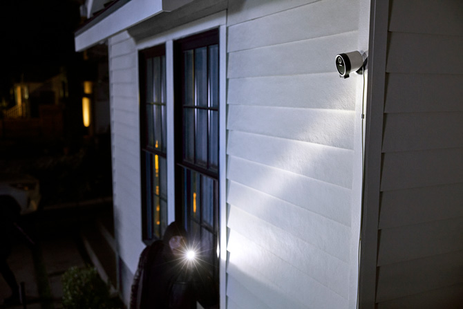 Outdoor scene with an intruder with a flashlight and a mounted outdoor security camera.