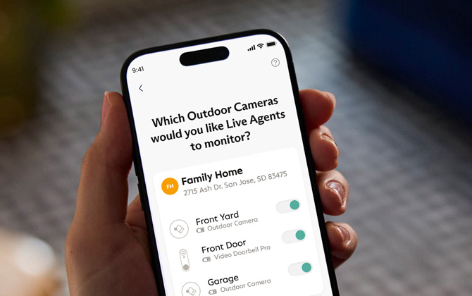 Phone with a screenshot of the SimpliSafe app showing the ability to activate sensors and cameras for different modes.