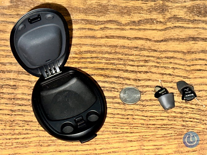 Sony CRE-10 OTC hearing aids show out of their case with a dime. The hearing aid on the left has the battery case door open.