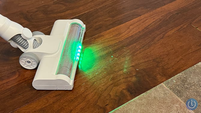 The SwitchBot K10+ Pro Combo stick vac LED light shows pet hair and dust on wood floor.