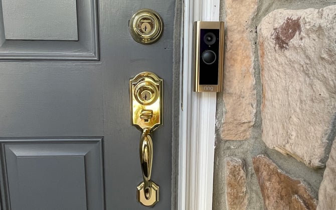 Picture of the Ring Video Doorbell 2  with brushed gold faceplate installed to the right of a gray door. You can see the door handle and lock. 