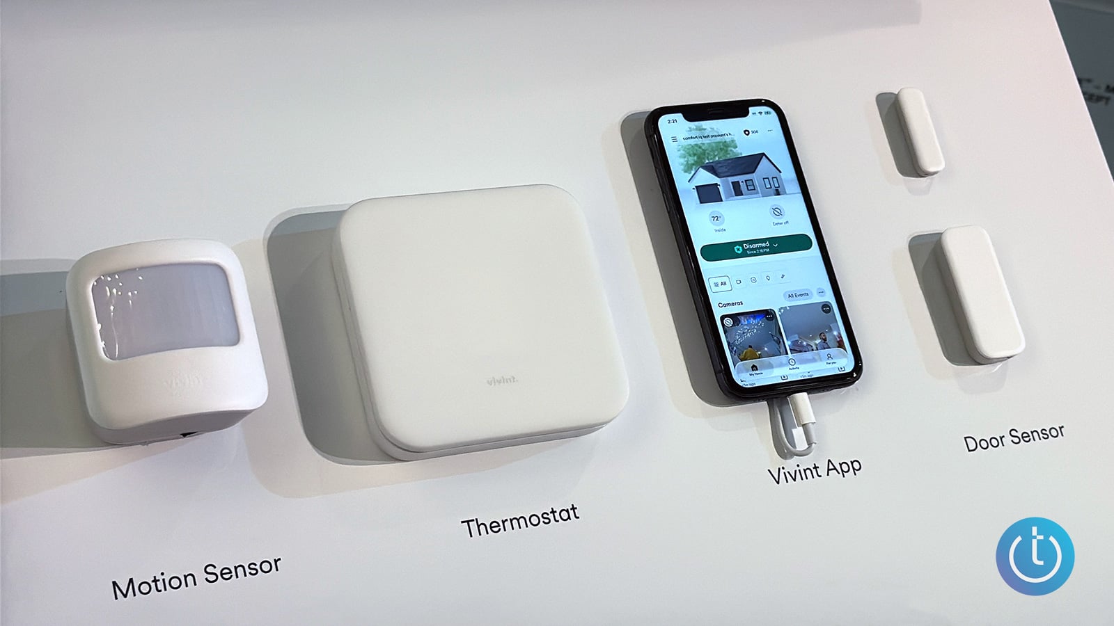 Vivint motion sensor, thermostat, smartphone displaying the Vivint app, and two-piece door sensor mounted on a labeled display board.