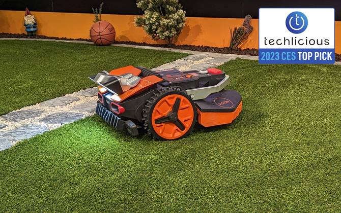 Worx Landroid Vision on grass near a stone path with obstacles in the background