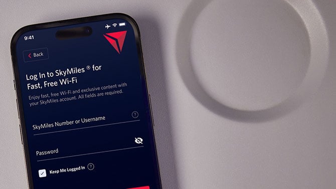 A phone showing the SkyMiles login screen sits on a airline tray table.