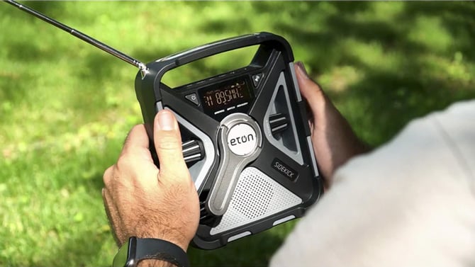 Eton Sidekick Weather Radio with Bluetooth shown held in two hands with the antenna raised.