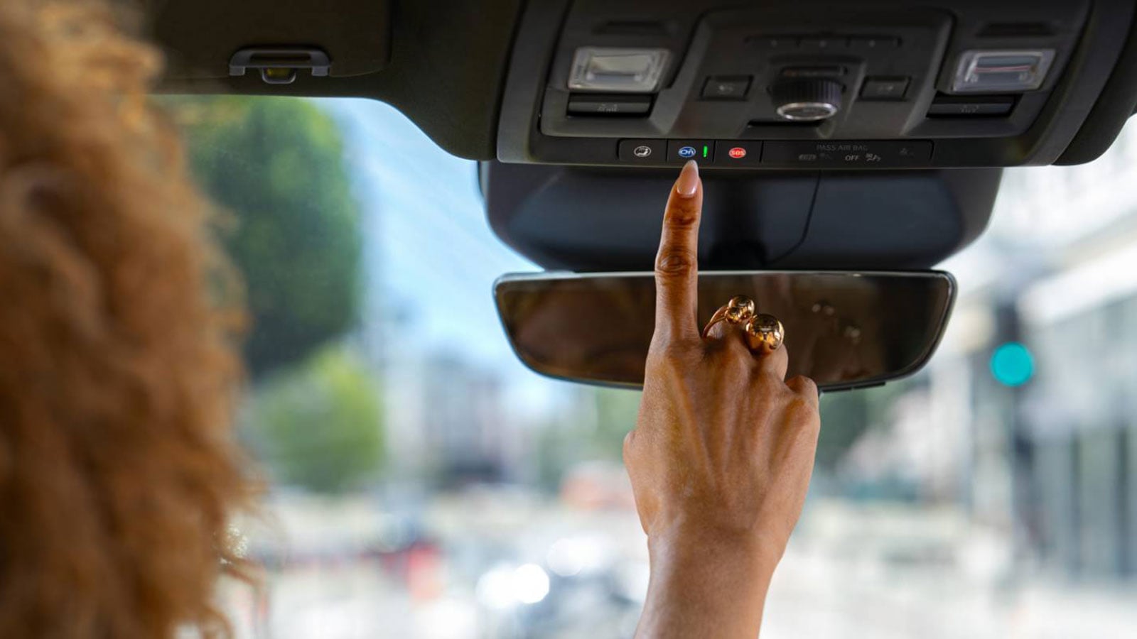 write alt text Woman pressing the blue OnStar button on the overhead console of a GM vehicle.