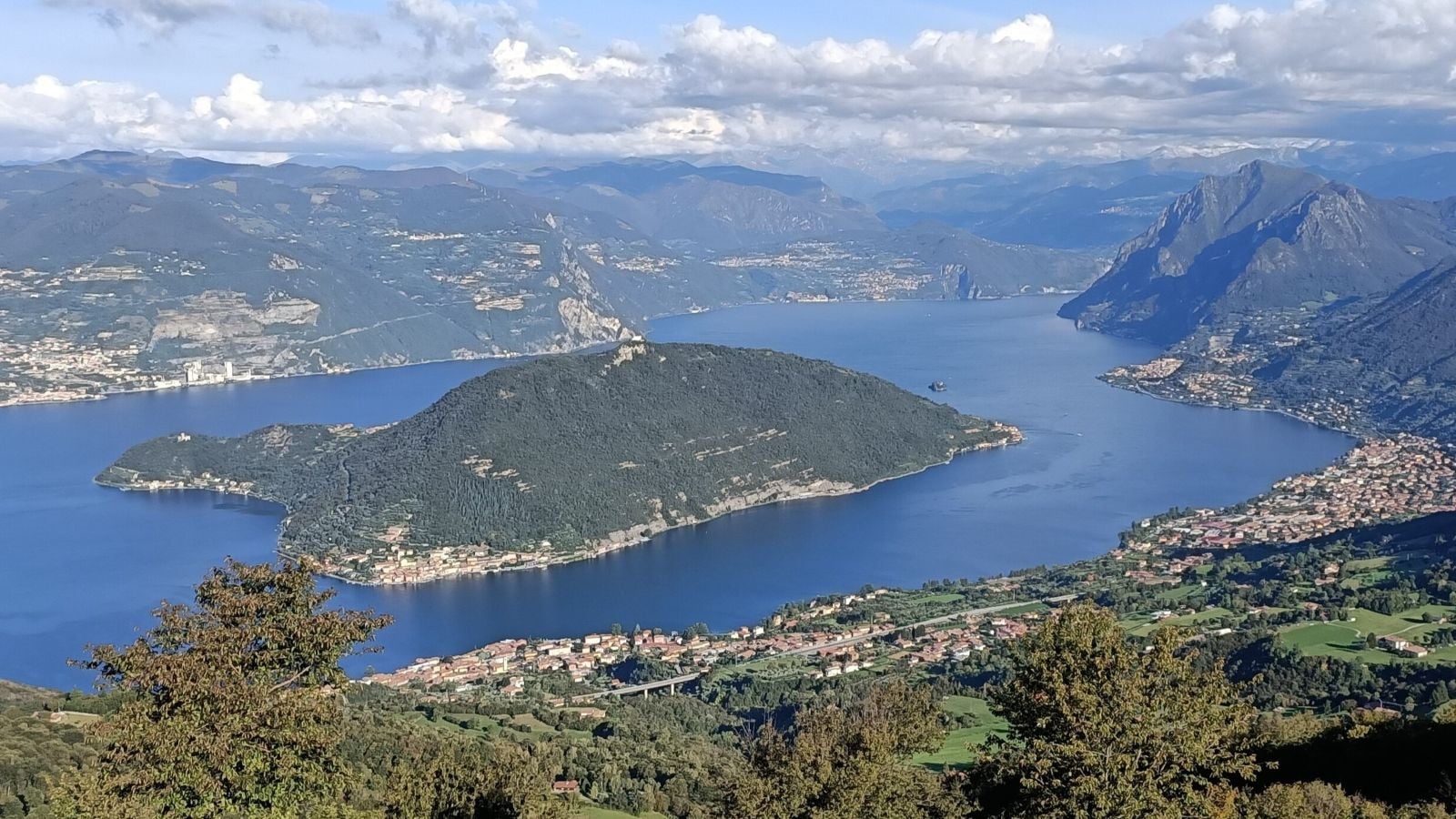 Panoramic view of Lake Iseo in northern Italy, surrounded by forested mountains and lakeside towns.