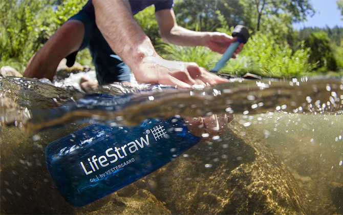 LifeStraw Go Water Filtering Bottle open and submerged in a stream. The the person's other hand is the top show the top with the filter straw.