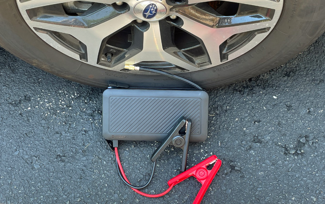 Mophie Powerstation Go Rugged with Air Compressor shown with jumper cables in front of a car tire.